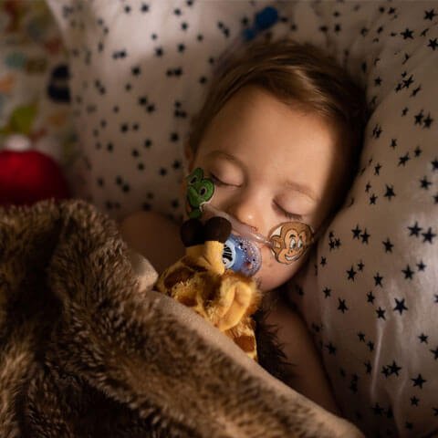 Baby girl with oxygen tube in bed cuddling a teddy
