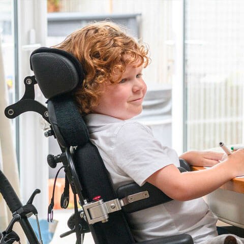 Boy in wheelchair at table while writing