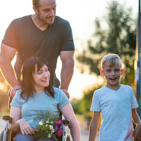 Man pushing a women in a wheelchair while she holds the hand of a boy walking next to her