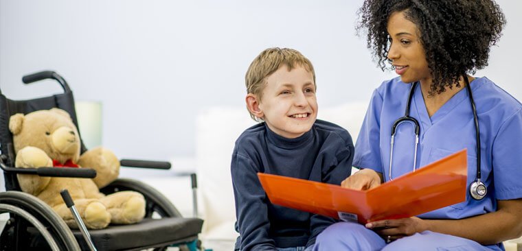 Healthcare worker with child looking at a folder. A wheelchair and teddy are in the background