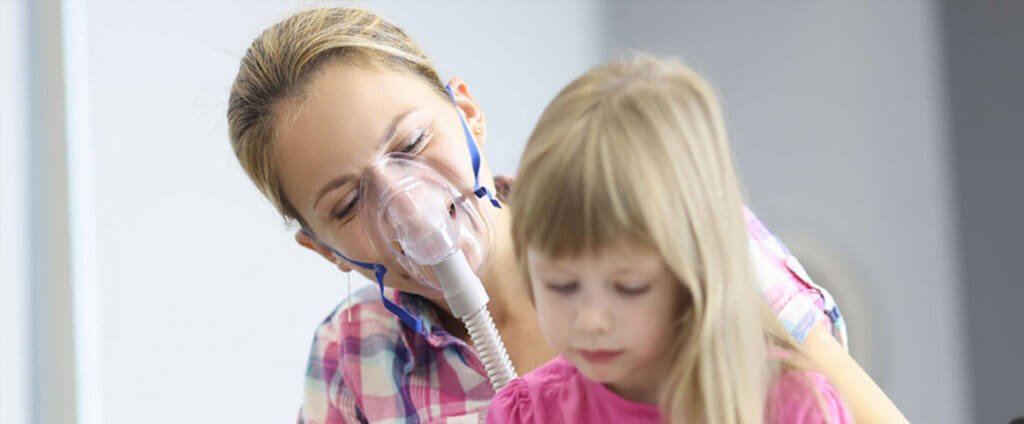 Women with breathing mask looking at child sitting on her lap in a wheelchair