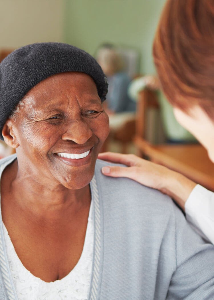 Women smiling at healthcare worker. The healthcare worker has her hand on the woman's shoulder